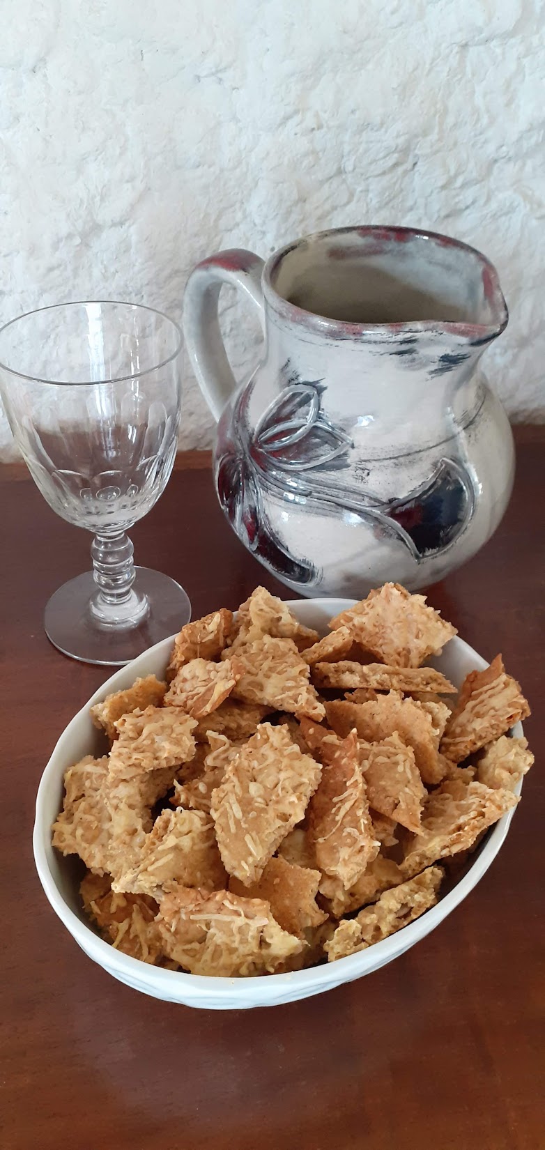 Cuisine à domicile - sur une table en bois un verre à pied, un pichet et un plat rempli de crackers maison